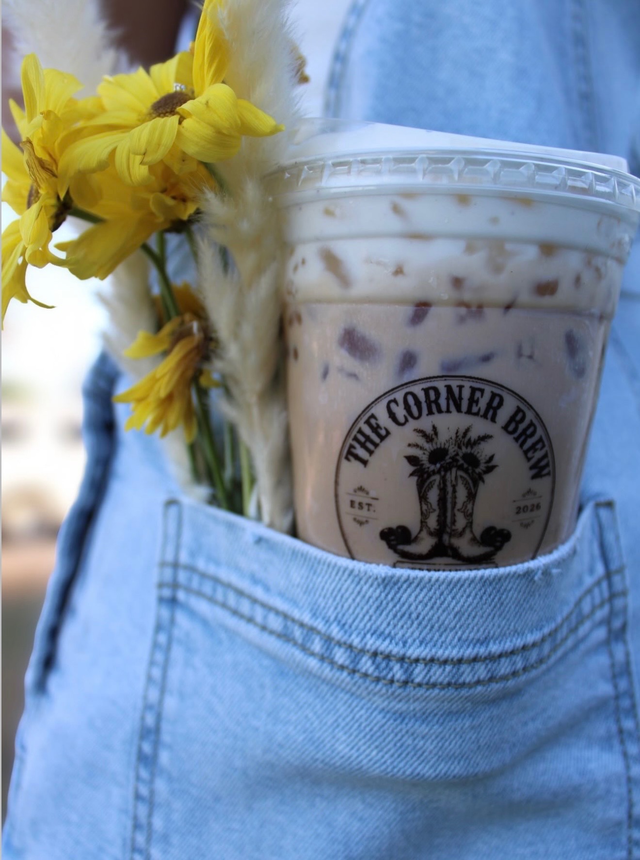 Iced Corner Brew coffee in a denim back pocket with yellow sunflowers.